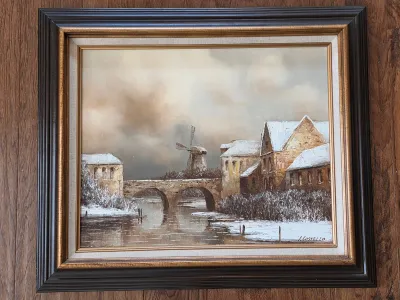 Framed oil painting of a winter landscape featuring a stone bridge, river, and windmill, signed by J. Costello, housed in a dark wood...