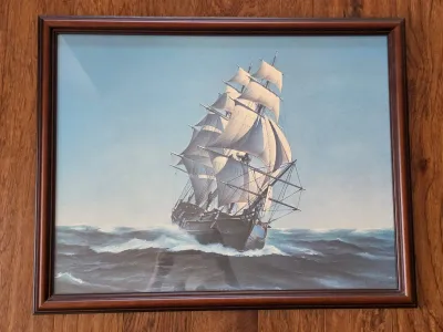 Framed maritime print depicting a multi-masted sailing ship navigating choppy seas, housed in a dark wood frame.