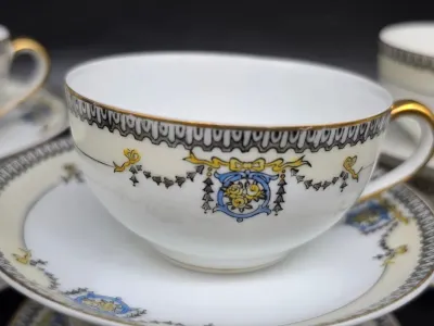 Vintage porcelain teacup and saucer set featuring a delicate yellow rose and blue ribbon motif with gold-gilded rims and handle.