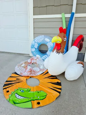 Assortment of pool toys including a large inflatable rooster float, several swim rings with tropical and alligator designs, and foam pool...