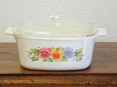 Corning Ware French Pansy pattern casserole dish with clear glass lid, featuring a colorful floral design on a white ceramic body.