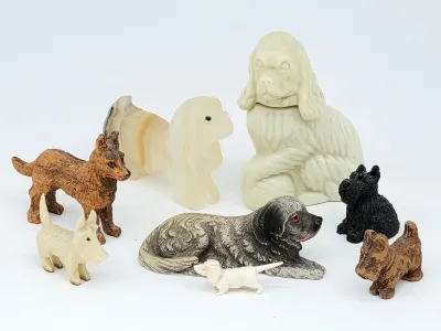 Collection of vintage miniature dog figurines in various materials, including carved stone, molded plastic, and textured resin, featuring...