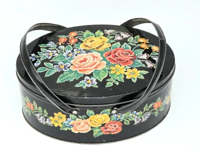 Vintage oval metal tin basket with a black background, featuring a colorful needlepoint-style floral design on the lid and sides,...
