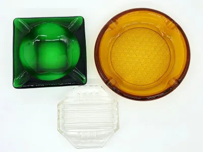 Trio of vintage glass ashtrays, including a square forest green piece, a large round amber glass piece with a textured center, and a...