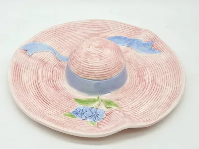 Vintage ceramic sun hat serving dish, featuring a pink textured brim, blue ribbon band, and floral accent.