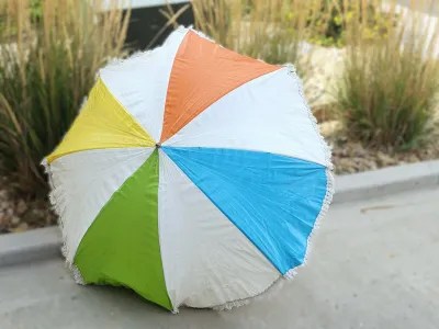 Vintage multi-colored beach umbrella featuring alternating panels of white, orange, blue, green, and yellow with a fringed border.