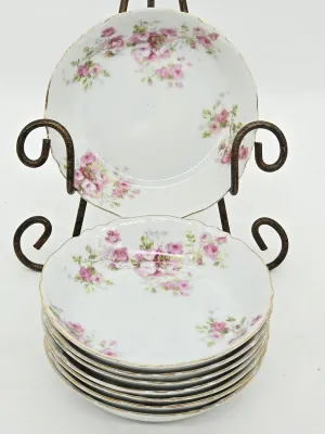 Set of vintage porcelain berry bowls featuring a delicate pink rose pattern with scalloped, gold-trimmed rims, displayed on a wrought...