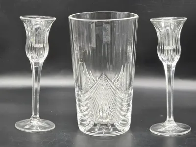 Three-piece clear crystal set featuring a tall cylindrical vase with a ribbed and chevron-cut pattern, flanked by a pair of matching...