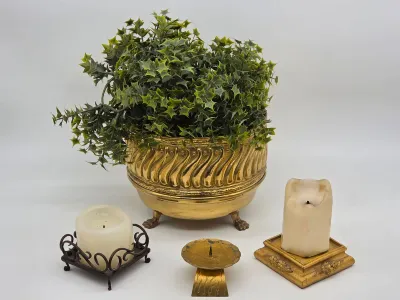 Vintage brass footed planter with faux greenery, accompanied by three assorted candle holders and pillar candles.