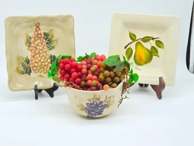 Tuscan-style ceramic kitchen decor set, featuring two square decorative plates with grape and pear motifs on display stands, paired with...