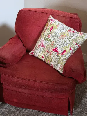 Upholstered red armchair with a skirted base, paired with a decorative throw pillow featuring a green and red birdhouse pattern.
