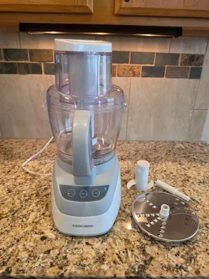 Black & Decker food processor with a white and grey base, clear work bowl, and accompanying slicing disc and blade attachments.