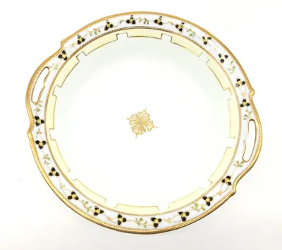 Vintage porcelain serving platter with handles, featuring a cream and gold geometric border accented with black and gold floral motifs.