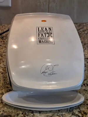 Vintage white George Foreman Lean Mean Fat Reducing Grilling Machine with matching drip tray, showing light wear from use.
