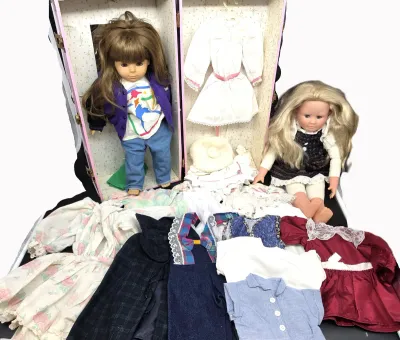 Vintage doll collection featuring two dolls, a pink wardrobe trunk, and an assortment of doll clothing and accessories, circa 1980s-1990s.