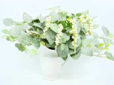 Faux floral arrangement featuring green and white nerve plant leaves and white wisteria blossoms in a white ceramic pitcher.