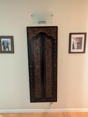 Ornate hand-carved wooden wall panel with double doors and intricate floral motifs, flanked by framed prints of an elephant and a...