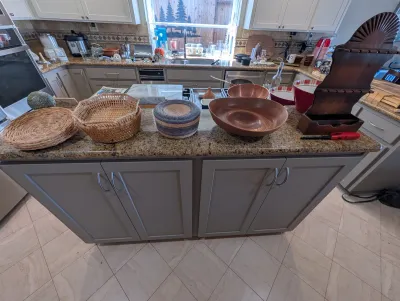 Assorted kitchenware and home decor items, including woven baskets, a large wooden bowl, and a vintage wooden wall shelf, displayed on a...