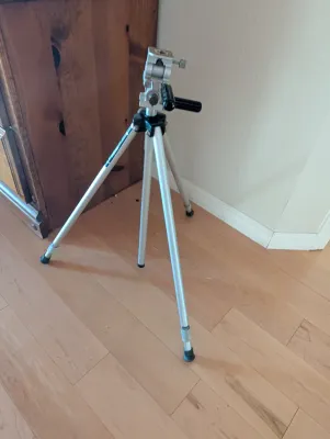 Vintage aluminum camera tripod with adjustable legs and pan-tilt head, showing some light wear from use.