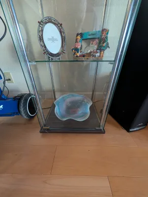 Modern glass display cabinet with chrome trim, housing decorative picture frames and an art glass bowl.