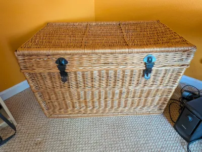 Large woven wicker storage trunk featuring a hinged lid and two black metal latches on the front.