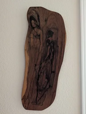 Vintage wood burning art on a live-edge wooden slab, depicting two stylized figures integrated into the natural wood grain.