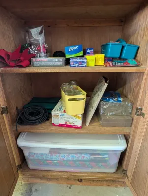 Wooden storage cabinet containing various household items, including kitchen wraps, Ball canning jars, a plastic storage bin with...