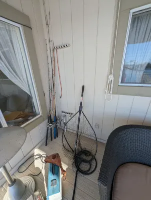 Assorted fishing gear including several vintage rods, a large landing net, and a tackle box on an outdoor patio.