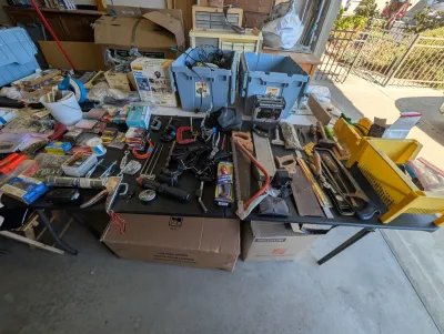 Assortment of hand tools, hardware, and garage items, including saws, clamps, a caulking gun, and storage bins, displayed on a folding...