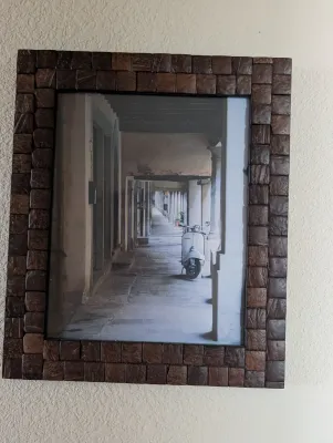 Framed photograph of a vintage motor scooter parked in a European-style colonnade, set in a rustic frame made of small wooden tiles.