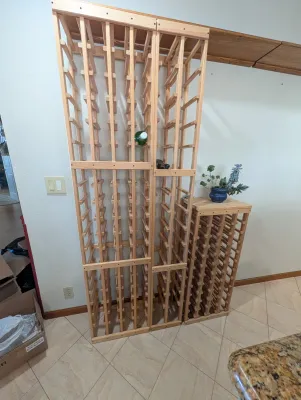 Modular light wood wine racks, including two tall vertical units and one shorter unit with a flat top surface.