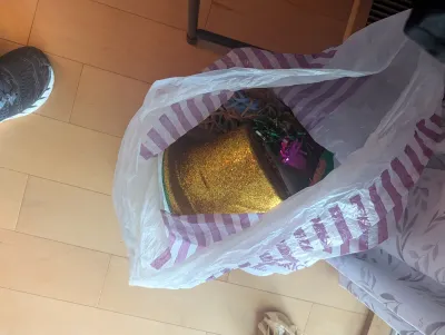 Assorted party supplies, including a gold glitter top hat and colorful decorations, stored inside a plastic shopping bag.