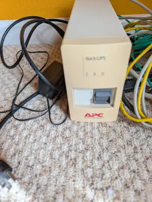 Vintage APC Back-UPS 280 uninterruptible power supply unit with associated power cords and cables.