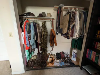 Closet filled with assorted men's and women's clothing, hats, and a variety of shoes lined up along the floor.