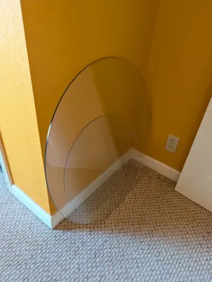 Two circular glass table tops in different sizes, leaning against a yellow wall.