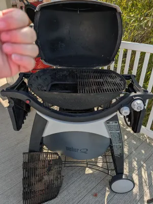 Weber Q series portable liquid propane gas grill on a wheeled cart, showing some wear and including an extra cooking grate.
