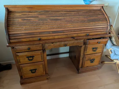 Vintage pine roll-top desk featuring a tambour door, multiple drawers with metal ring pulls, and a central lap drawer.