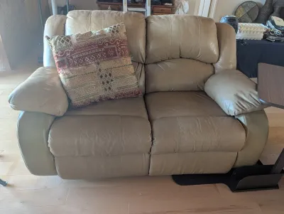 Contemporary tan leather reclining loveseat with plush armrests and a patterned accent pillow.