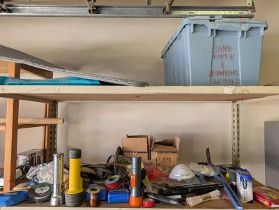 Assorted garage items on shelving, including flashlights, tape, a dust mask, and a storage bin labeled "Sandpaper & Painting...