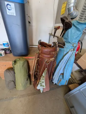 Vintage golf bags, including a brown leather bag and a light blue vinyl bag, containing a selection of vintage wood and iron golf clubs.