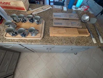 Assorted kitchenware including a set of seven hand-painted stoneware mugs on a wooden tray, bamboo drawer dividers in boxes, and large...