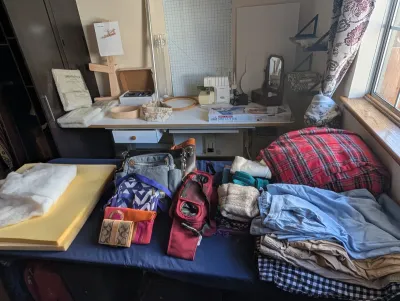 Assorted craft supplies, sewing notions, and clothing items, including a Logan mat cutter, a sewing machine, various handbags, and folded...