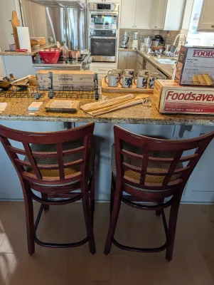 Pair of cherry-finished wooden barstools with grid-patterned backs and upholstered seats, shown alongside various kitchenware items...