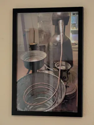 Framed photograph depicting an antique copper still and distillation equipment, presented in a simple black frame.
