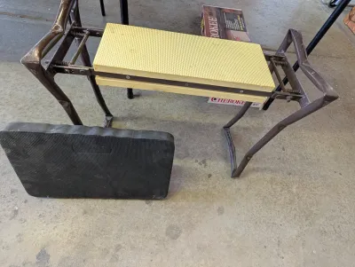 Vintage folding garden kneeler and bench with a yellow foam pad, accompanied by a black foam kneeling pad.