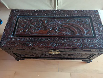 Ornate hand-carved camphor wood chest featuring a detailed peacock and floral motif on the lid, complete with a brass latch.