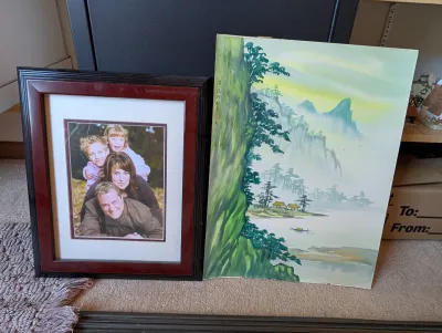 Framed family portrait in a dark wood frame alongside an unframed East Asian landscape painting on paper depicting mountains, water, and...