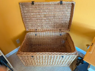 Large vintage woven wicker storage trunk with a hinged lid and metal hardware, showing some light wear consistent with age.