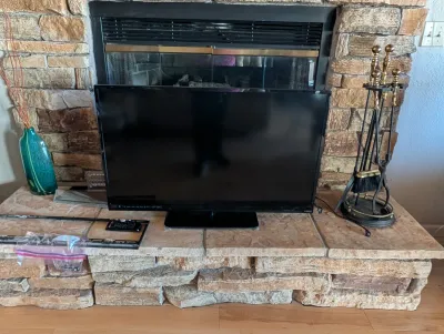 Vizio flat-screen television on a stand, accompanied by a remote control and mounting hardware, displayed on a stone fireplace hearth.