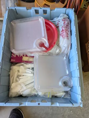 Light blue plastic storage tote filled with party supplies, including clear plastic appetizer plates with built-in cup holders, red paper...